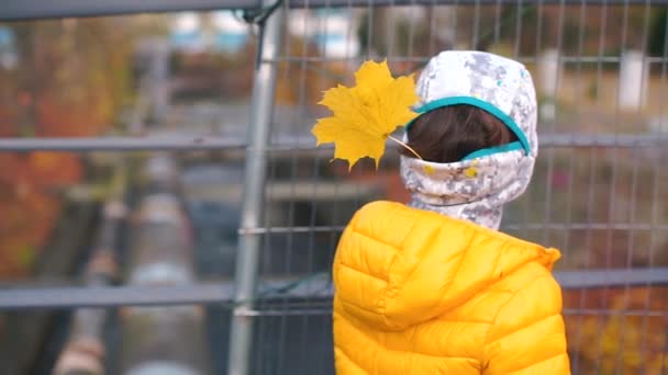 Um menino de roupas amarelas fica de costas para a câmera — Vídeo de Stock