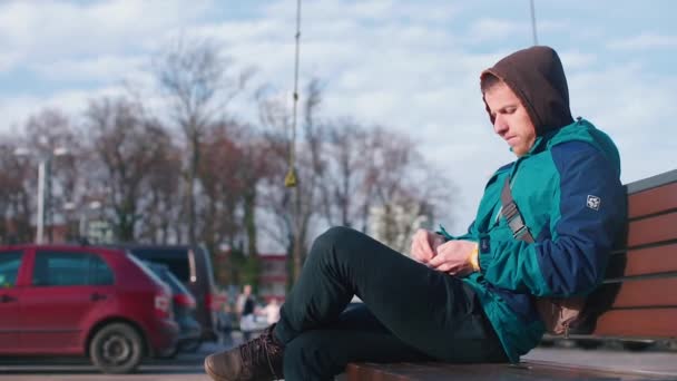 Парень делает домашнюю сигарету, сидя на скамейке на улице. . — стоковое видео