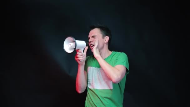 En man i gröna kläder skriker i en megafon på svart bakgrund. — Stockvideo