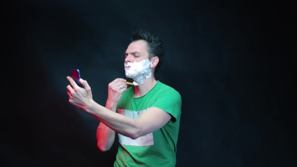 Muž si holí obličej, když se dívá na obrazovku smartphonu. — Stock video