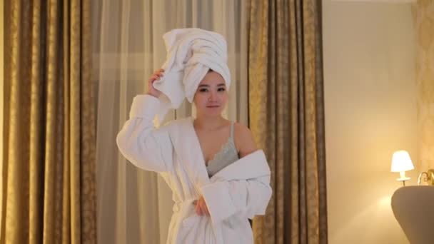 An Asian girl is standing in the bedroom in a white bathrobe. — Stock Video