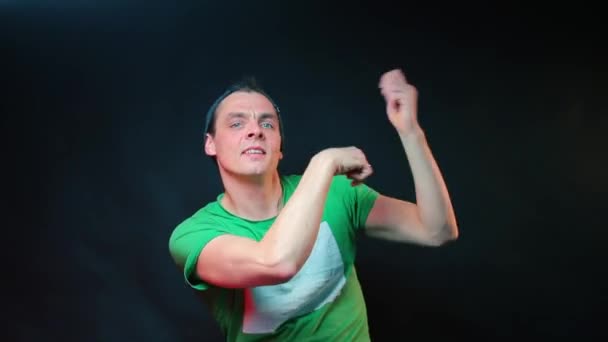 Un gars en vêtements verts fait des mouvements de danse avec ses mains . — Video