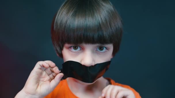 The boy peels off adhesive tape from his mouth. — Stock Video