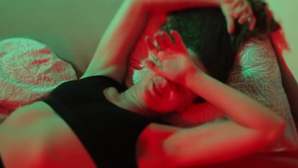 Een vrolijke vrouw ligt in bed in rood licht. — Stockvideo