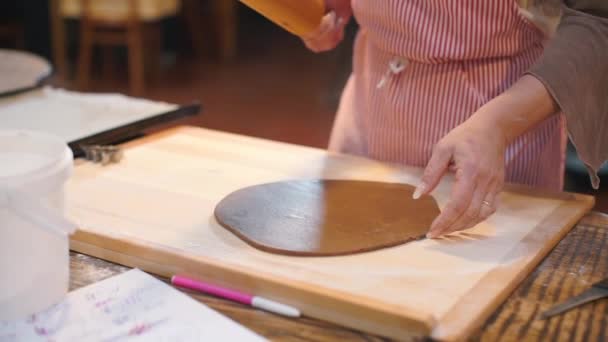 Granjero rueda masa marrón con un rodillo en una tabla de madera con sus manos . — Vídeos de Stock