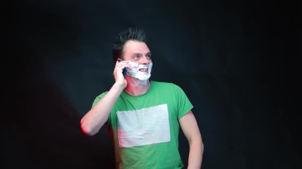 A man with shaving foam on his face is talking on a cell phone. — Stock Video