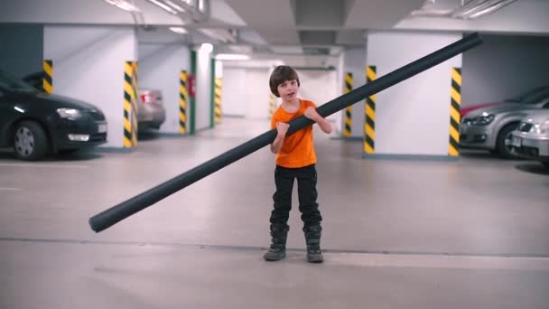 Мальчик с длинной трубой в руках стоит в гараже . — стоковое видео