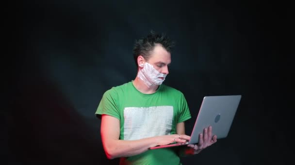 A man with shaving foam on his face is using a laptop. — ストック動画