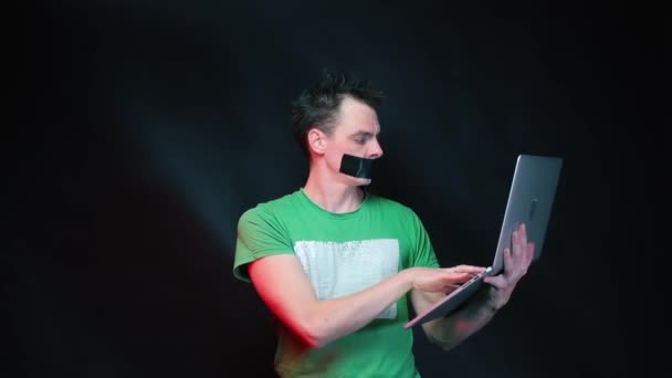 Ein Büroangestellter arbeitet an einem Laptop mit einem mit schwarzem Klebeband verschlossenen Mund. — Stockvideo
