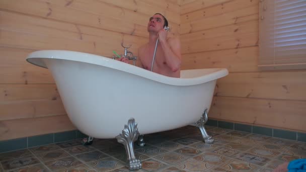 男はシャワーの下の浴室に座っている間に歯を磨く. — ストック動画