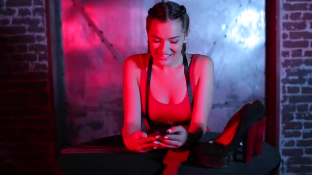 Une fille dans une boîte de nuit se tient à une table et utilise un smartphone — Video
