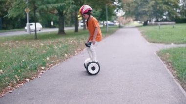 İtfaiyeci kaskı takmış bir çocuk patika boyunca segway sürüyor.