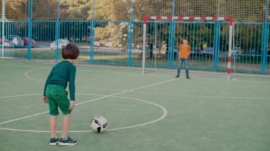 Bir okul çocuğu kalede bir futbol topuna vurur, ikinci bir öğrenci topu yakalar.