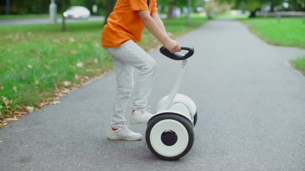 Teenager in an orange T-shirt on a background of cars stands on a gyroscooter — Stock Video