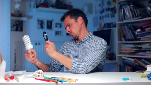 Mann untersucht eine Glühbirne durch ein Vergrößerungsglas, legt eine Hand wie — Stockvideo