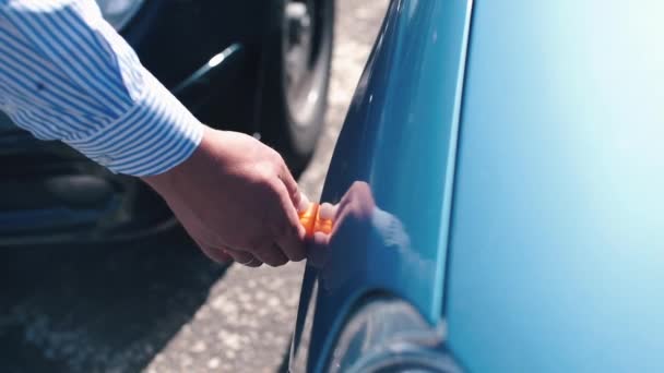 Un hombre hace una medición de la pintura y el metal de un coche usado — Vídeos de Stock