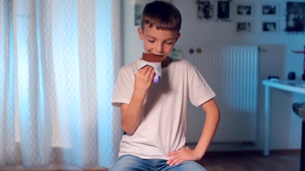 Écolier assis sur une chaise manger du chocolat — Video