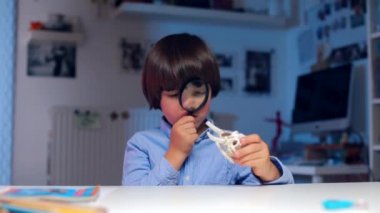 Okul çocuğu hayvan kemiklerini büyüteçle inceliyor.