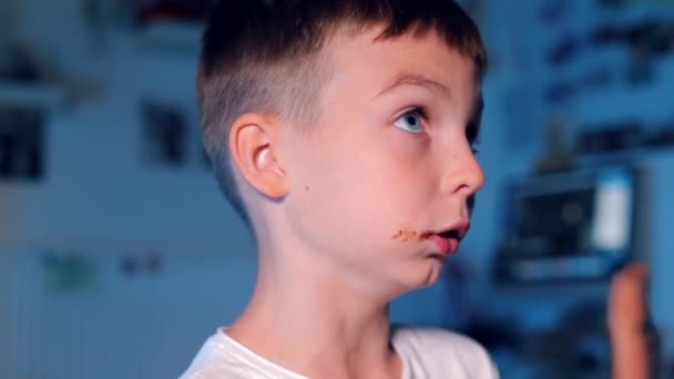 Мальчик, который жует шоколад на синем фоне — стоковое видео