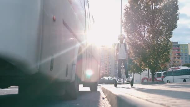 Хлопчик їде на півдорозі біля автобуса на фоні сонця — стокове відео