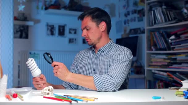 A man looks at a light bulb through a magnifying glass, shows surprise — Stock Video