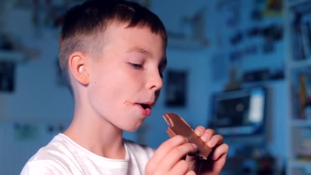 Adolescente comendo barra de chocolate em um fundo azul — Vídeo de Stock