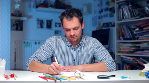 Der Mann am Tisch schreibt Text auf Papier, blickt vorsichtig in die Kamera — Stockvideo