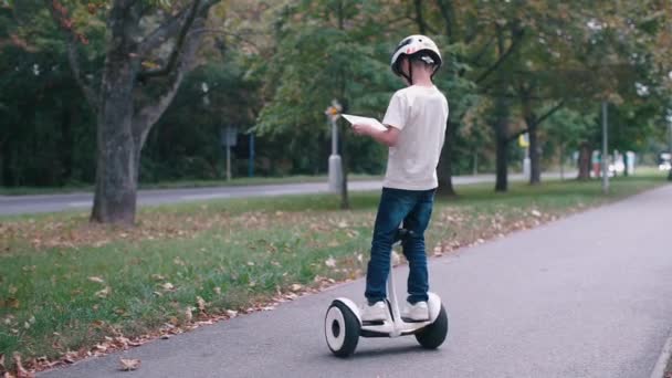 Chlapec se podívá na obrazovku tabletu, jezdí na gyroskútru — Stock video