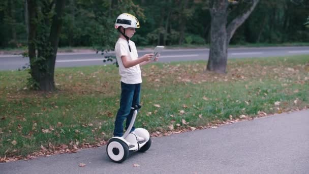 Criança moderna usa um tablet gadget em pé em um segway — Vídeo de Stock