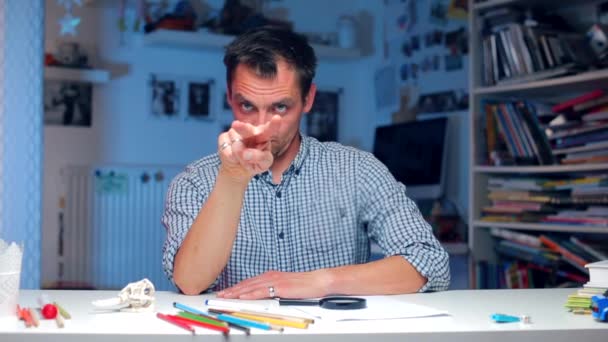 Un hombre sentado en la mesa muestra un gesto mirándote — Vídeos de Stock