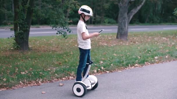 De jongen gebruikt een tablet, rijdt op een gyroscooter — Stockvideo