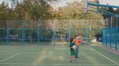 İki okul çocuğu okul bahçesindeki basketbol sepetine top atıyor.