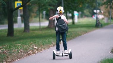 Bir çocuk segway 'de duruyor, sırt çantasından bir tablet alıyor.