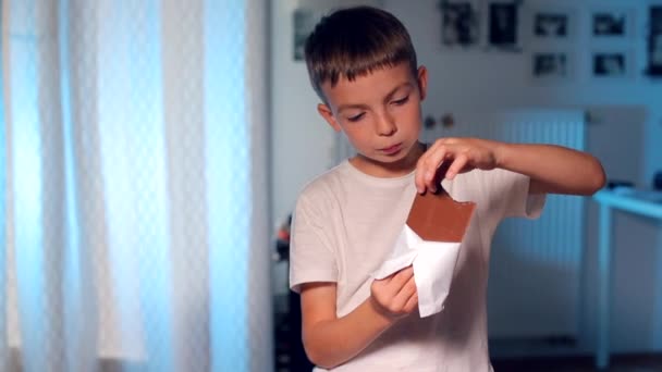 Il bambino mangia una barretta di cioccolato, rompe un pezzo con la mano — Video Stock