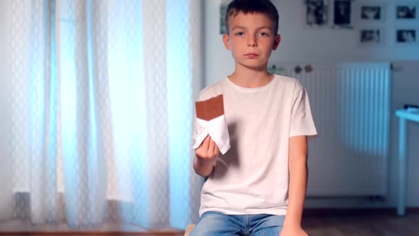 Nyugodt fiú ül egy etetőszéken fiú eszik egy csokoládé bár — Stock videók
