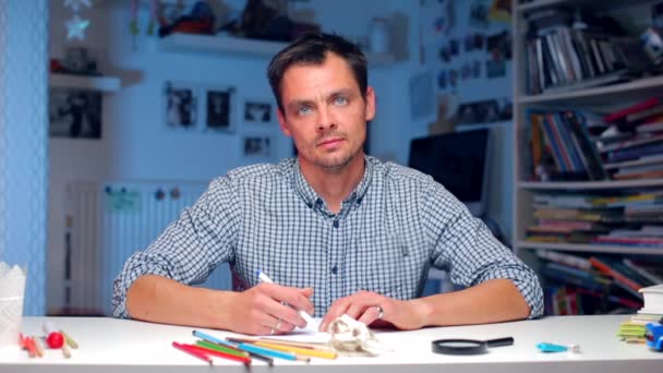 Чоловік сидить за столом пише текст на папері — стокове відео