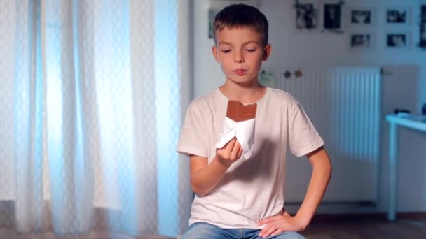 Jongen zit op een stoel en eet chocolade — Stockvideo