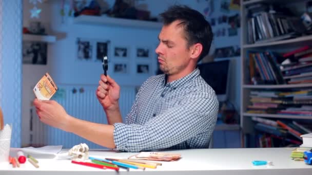 A man at a table examines a 50 euro bill through a magnifying glass — Stock Video