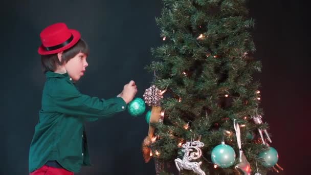 Um menino pendura um brinquedo em uma árvore de Natal . — Vídeo de Stock