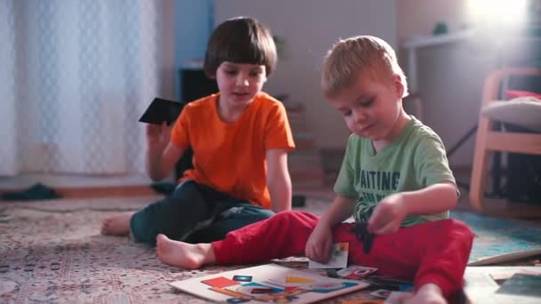 Two brothers sitting on the floor at home playing with baby cards. — Stock Video