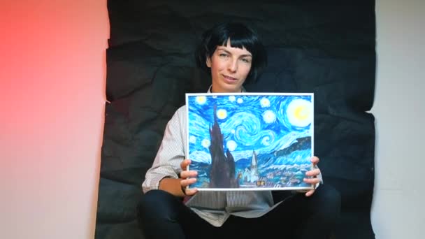Una bloguera está sosteniendo una foto dibujada por ella misma sobre un fondo negro . — Vídeo de stock