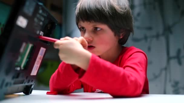 Um menino de roupas vermelhas coloca uma caneta na parte de trás de um laptop . — Vídeo de Stock