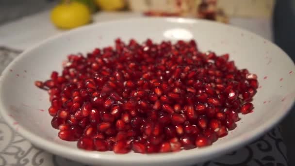 Granos de granada yacen en un plato blanco sobre la mesa — Vídeo de stock