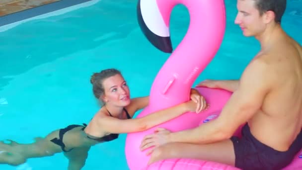 Chico con una chica flotando en el flamenco en la piscina — Vídeos de Stock