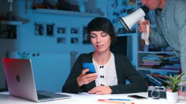 Masanın yöneticisi akıllı telefon kullanıyormuş. Yakınlarda, bir adam megafona bağırıyor..
