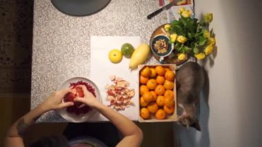 Narı bir tabakta temizliyor, yanında bir kedi yürüyor, mandalinalar uzanıyor.