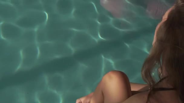 Девушка в купальнике сидит на краю бассейна — стоковое видео