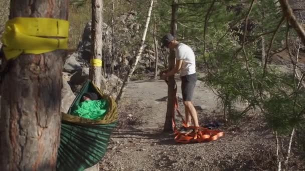 A guy is preparing a slackline line to tie a tree — 비디오