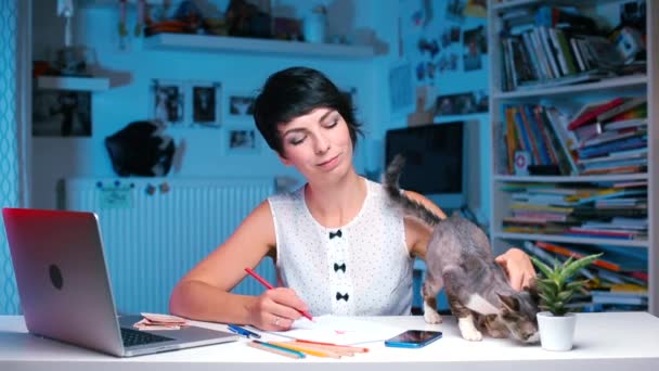 Το κορίτσι κάθεται στο τραπέζι και φτερνίζεται. Μια γάτα περπατάει γύρω από το τραπέζι — Αρχείο Βίντεο