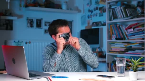 En man vid kontorsbordet tar bilder på en gammal kamera. — Stockvideo